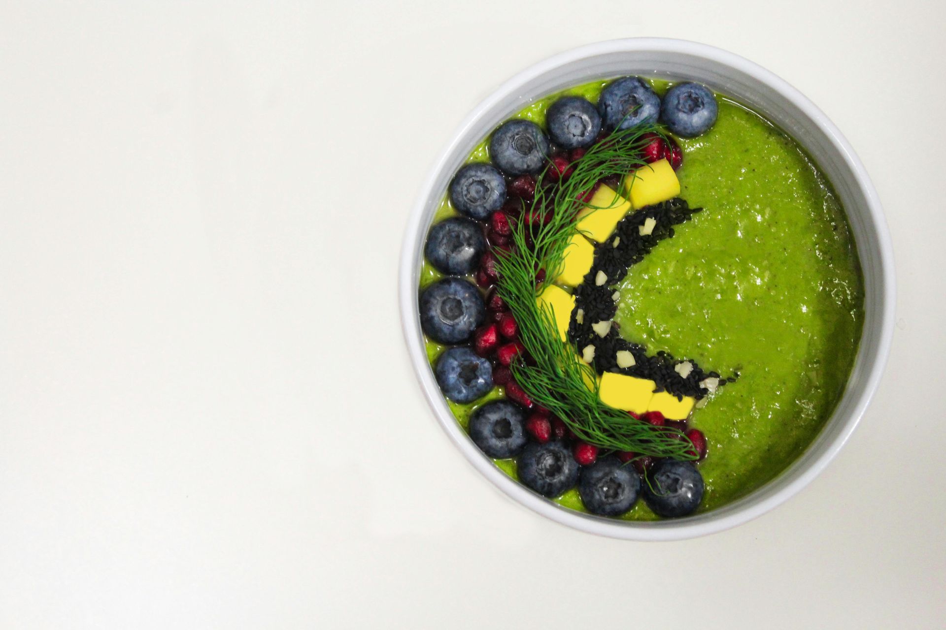 Green smoothie bowl decorated with blueberries, pomegranate, and a mango butterfly