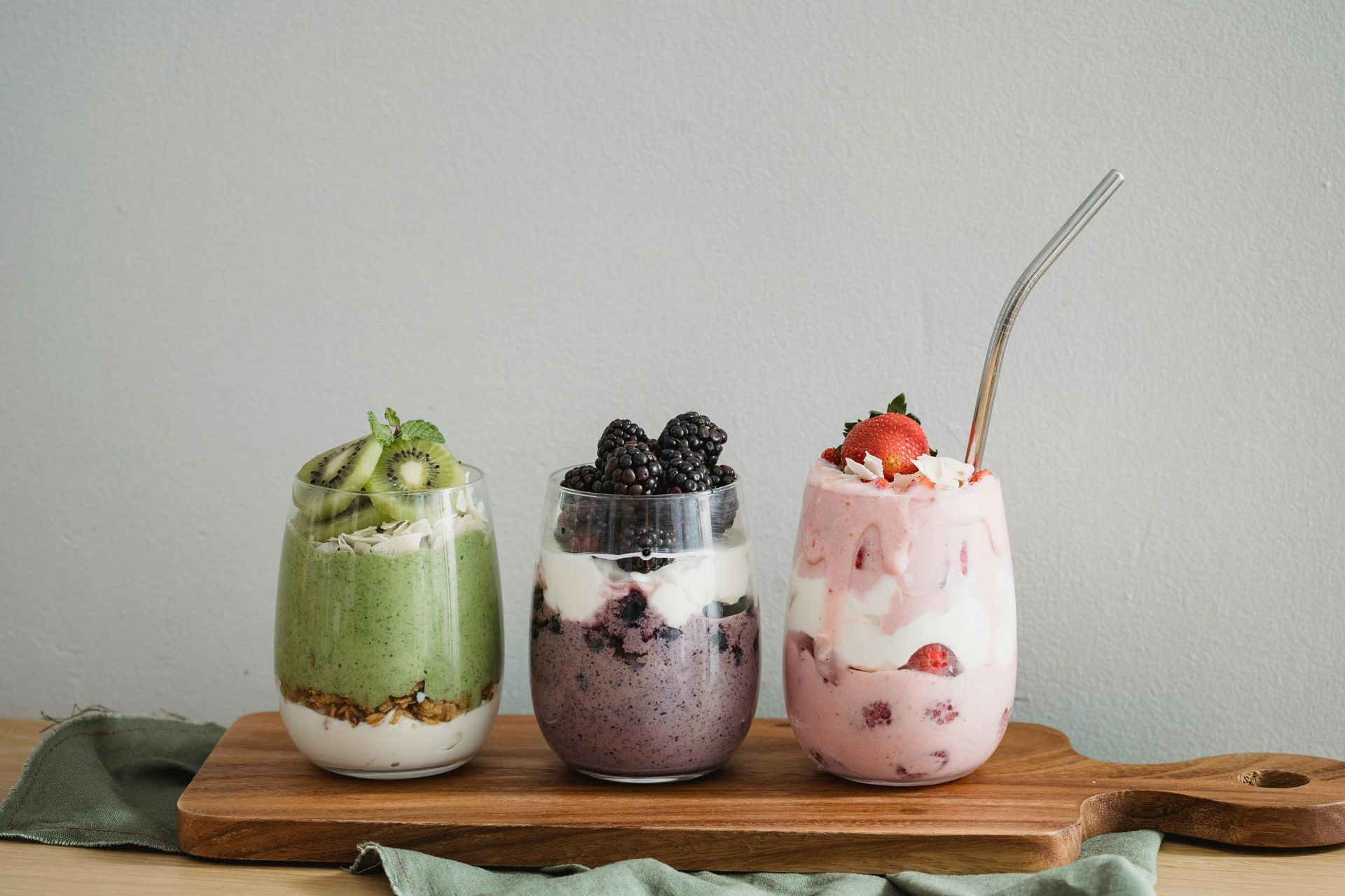 Three layered fruit smoothies in glass cups on a wooden board